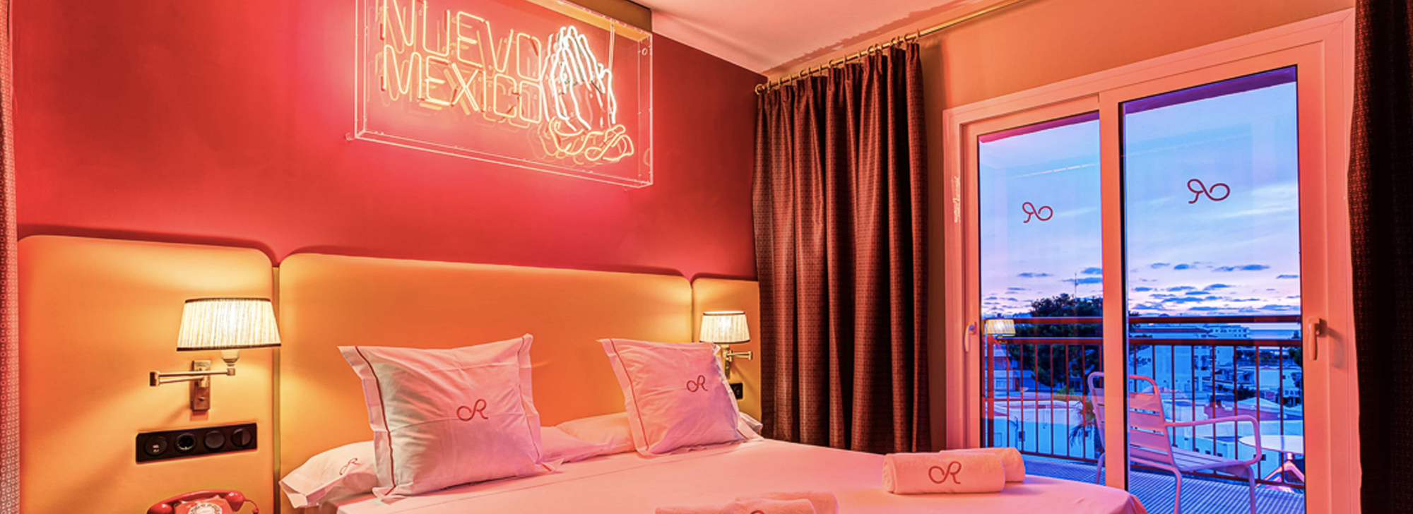 Bed in red, retro hotel room with neon 'Mexico City' sign